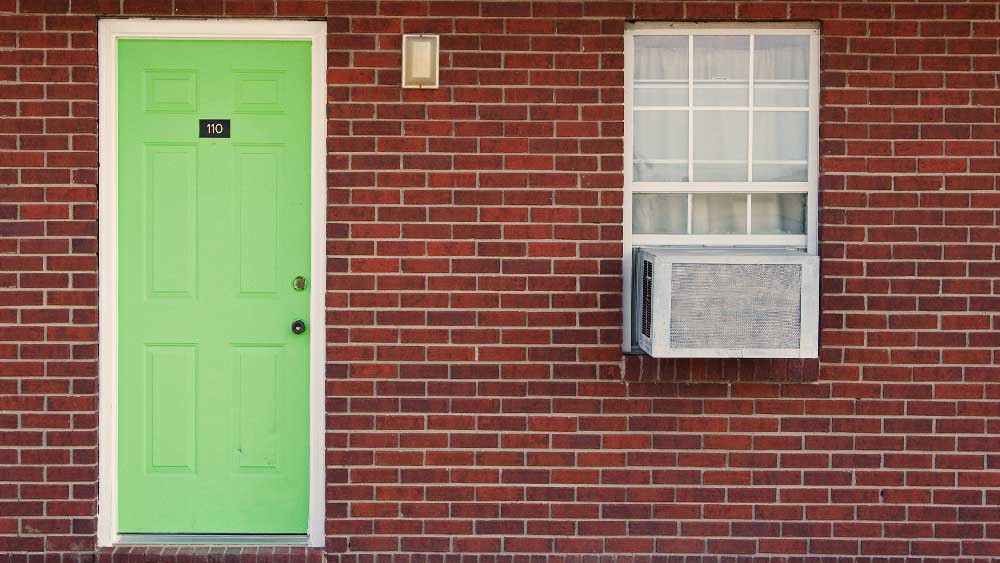 Ventana de aire acondicionado instalada en una casa de paredes rojas con una puerta verde loro